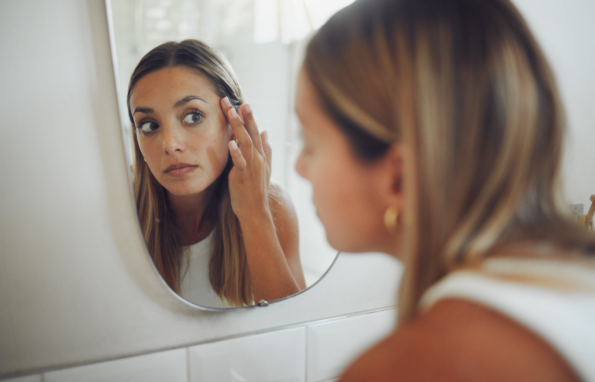 Woman examining dark spots and uneven skin tone in a mirror before hyperpigmentation treatment in Katonah, NY
